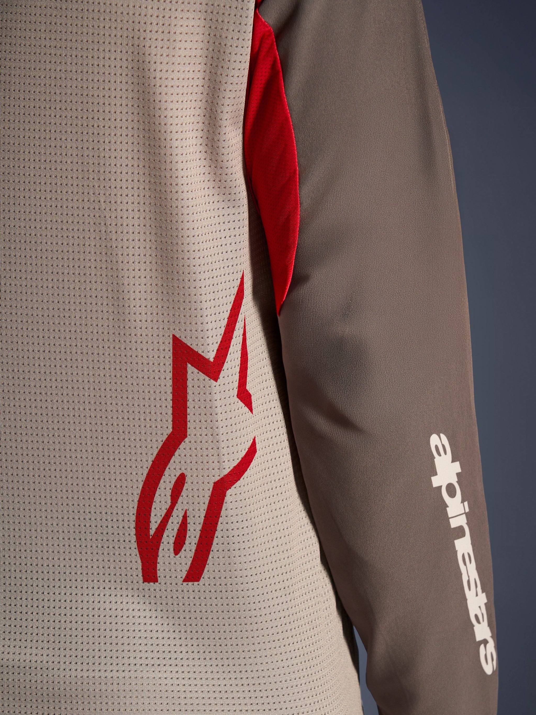 Alpinestars Maxdura Dual Jersey, Aluminum Walnut, close-up view showing the ventilated mesh torso with a red star logo and a brown abrasion-resistant sleeve with a white Alpinestars wordmark, technical adventure and dual-sport motorcycle apparel
