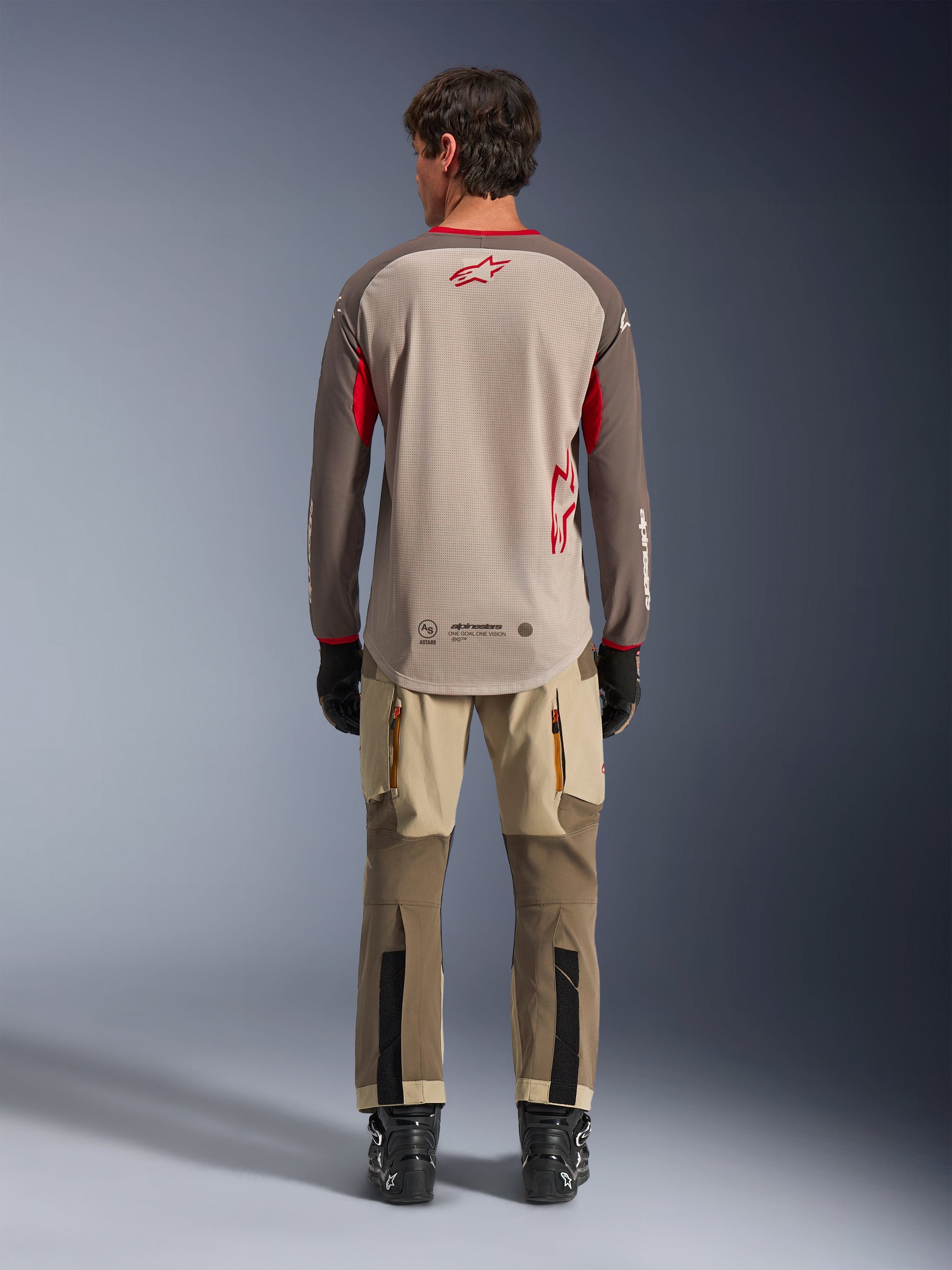 Alpinestars Maxdura Dual Jersey in Aluminum Walnut, back view, tan mesh torso with brown sleeves and red logos, dropped rear hem, paired with adventure riding pants and black boots.