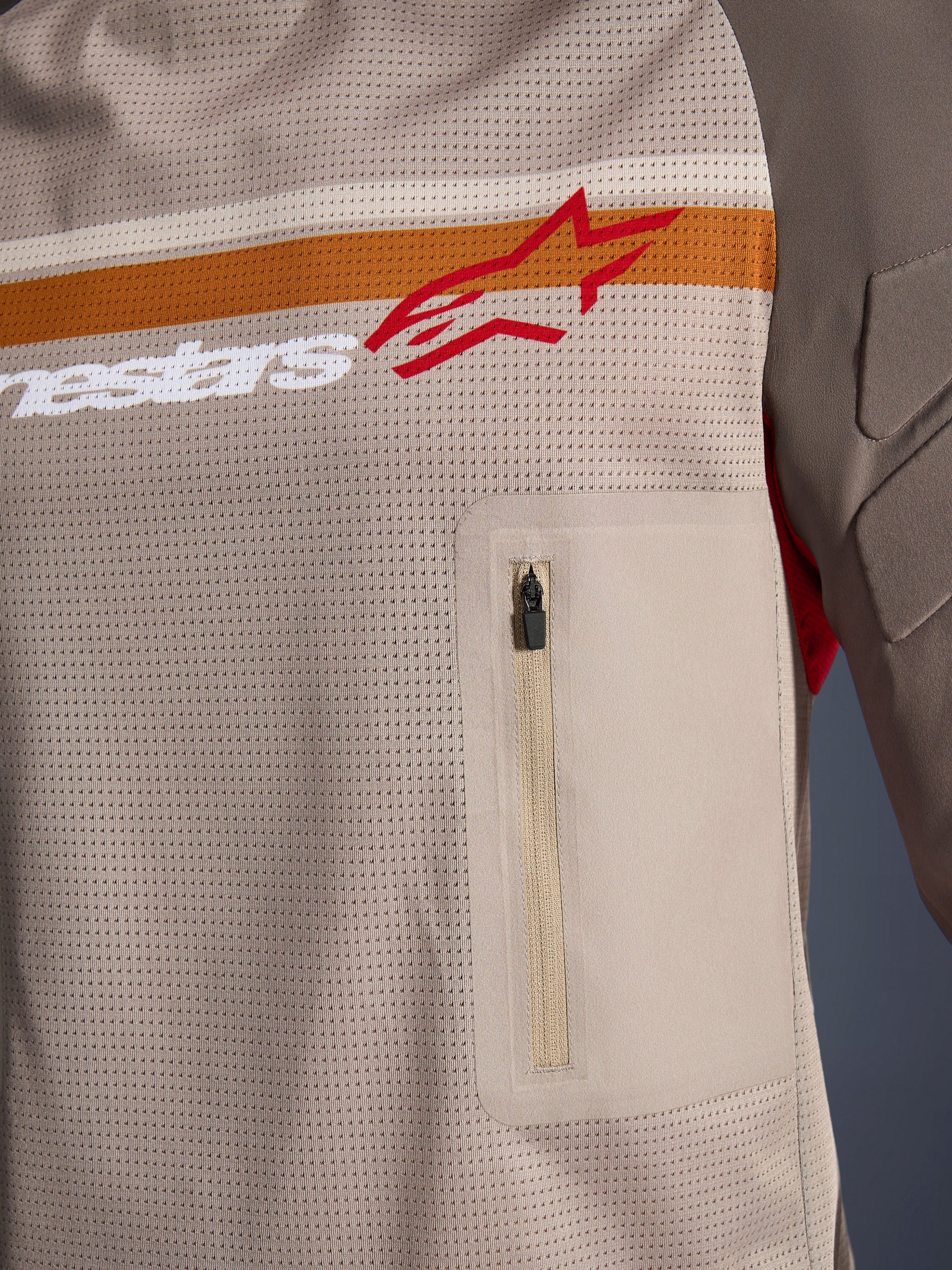 Alpinestars Maxdura Dual Jersey, Aluminum Walnut, close-up detail of the mesh torso, horizontal orange and white stripe with red logo, vertical zippered chest pocket, adventure motorcycle apparel