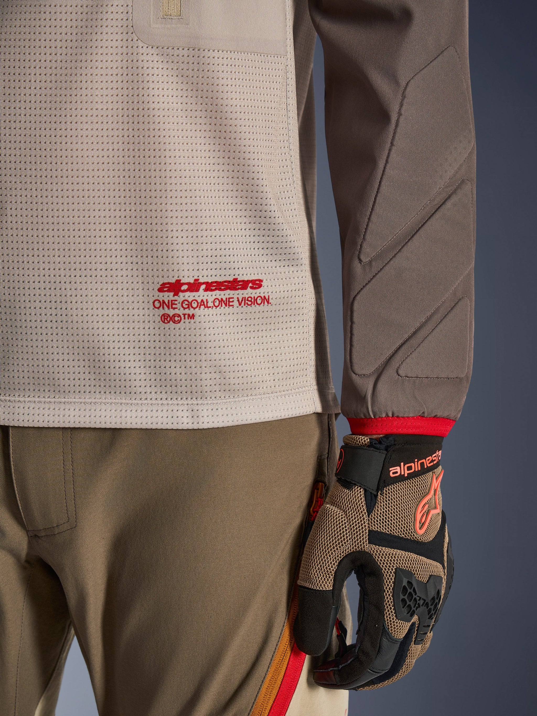 Alpinestars Maxdura Dual Jersey in Aluminum Walnut, detailed view showing the ventilated mesh torso with red branding, abrasion-resistant sleeve with integrated padding, worn with coordinated adventure riding pants and gloves
