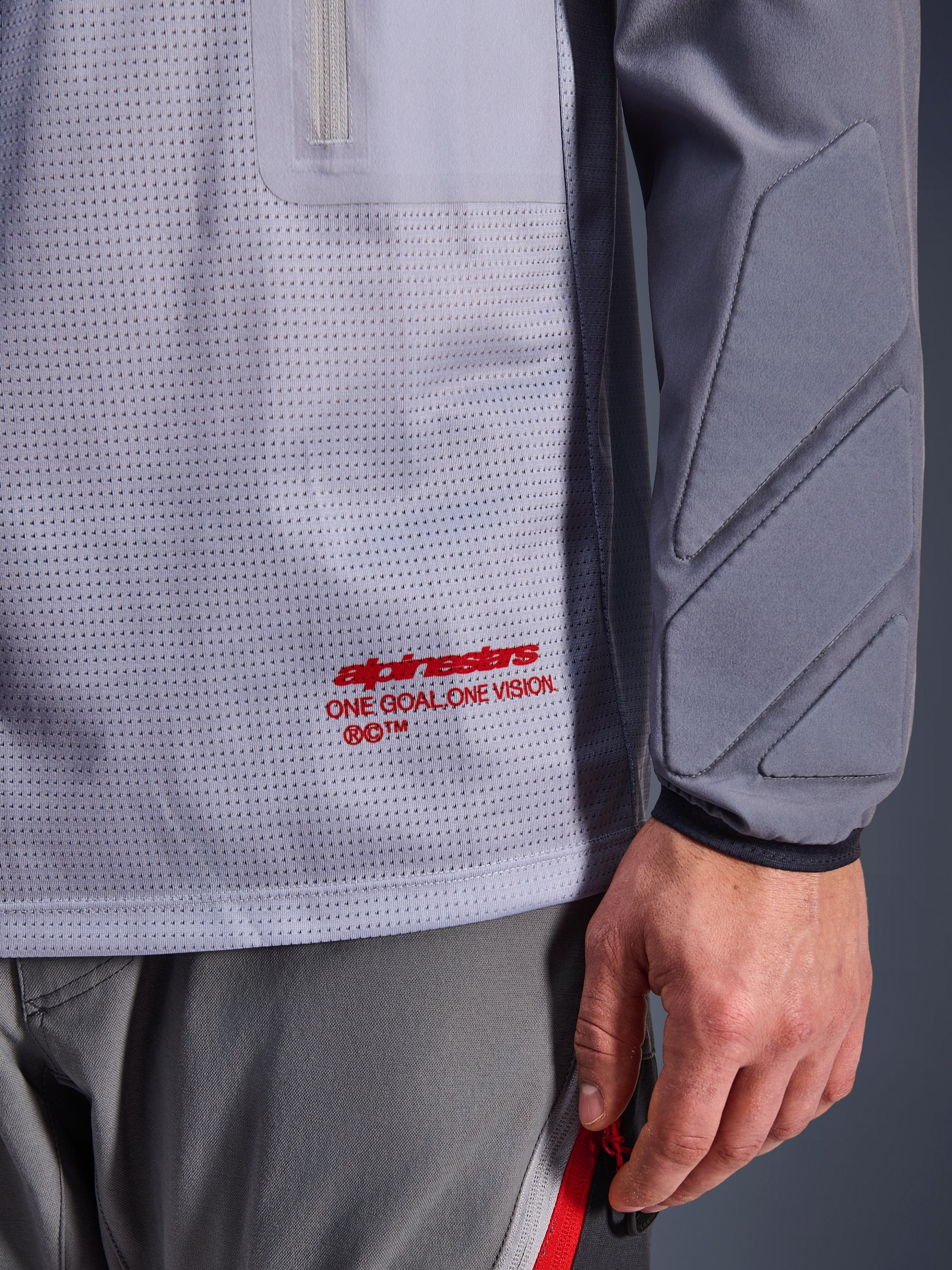 Alpinestars Maxdura Dual Jersey, Mid Gray and Dark Gray, close-up showing breathable mesh torso with red branding, zippered pocket detail, and integrated padding on the sleeve, technical adventure motorcycle gear