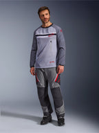 A man wearing the Alpinestars Maxdura Dual Jersey in Mid Gray and Dark Gray, styled with coordinating gray and black adventure pants and black boots, featuring a breathable mesh torso, zippered chest pockets, and red logo accents.