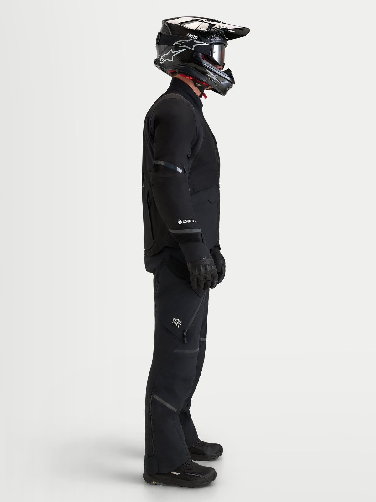 Alpinestars St-7 V2 2L Gore-Tex Jacket, Men's black waterproof adventure motorcycle jacket worn with matching pants, helmet, and riding gear, showing a side view profile