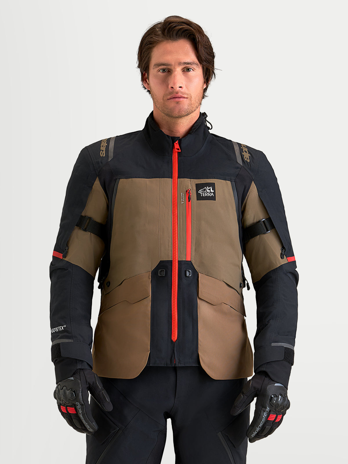 Alpinestars St-7 V2 2L Gore-Tex Jacket, men's adventure touring motorcycle jacket in walnut and black, featuring a waterproof GORE-TEX shell, bright red central zipper, and CE Level 2 armor, worn by a male model