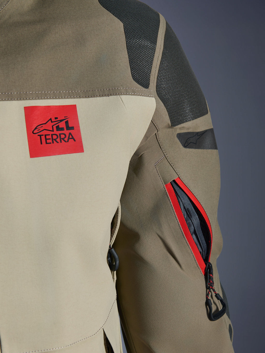 Alpinestars Nazca 3L GORE-TEX PRO Jacket, Walnut Rock Brown, detail of the back shoulder and sleeve, red 'ALL TERRA' logo patch, textured black Superfabric shoulder panels, zippered arm vent with red trim, premium adventure motorcycle apparel.