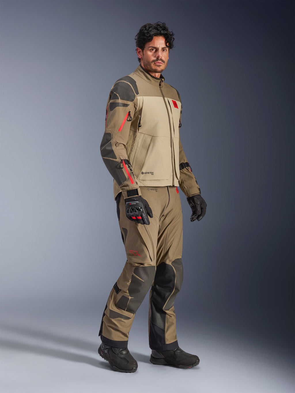 Alpinestars Nazca 3L GORE-TEX PRO Jacket, Walnut Rock Brown, adventure motorcycle riding jacket worn with matching pants and black gloves, featuring dark gray reinforcements, red zipper details, and a high-performance laminated shell.
