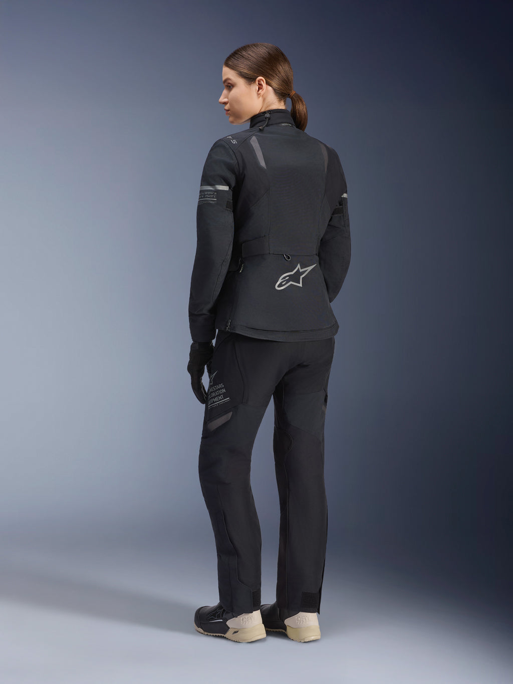 Women Stella ST-7 2L GORE-TEX Jacket, Black and Dark Gray, adventure touring jacket shown from the back, worn with matching black pants and cream boots, featuring the Alpinestars logo on the lower back, designed for all-season road touring