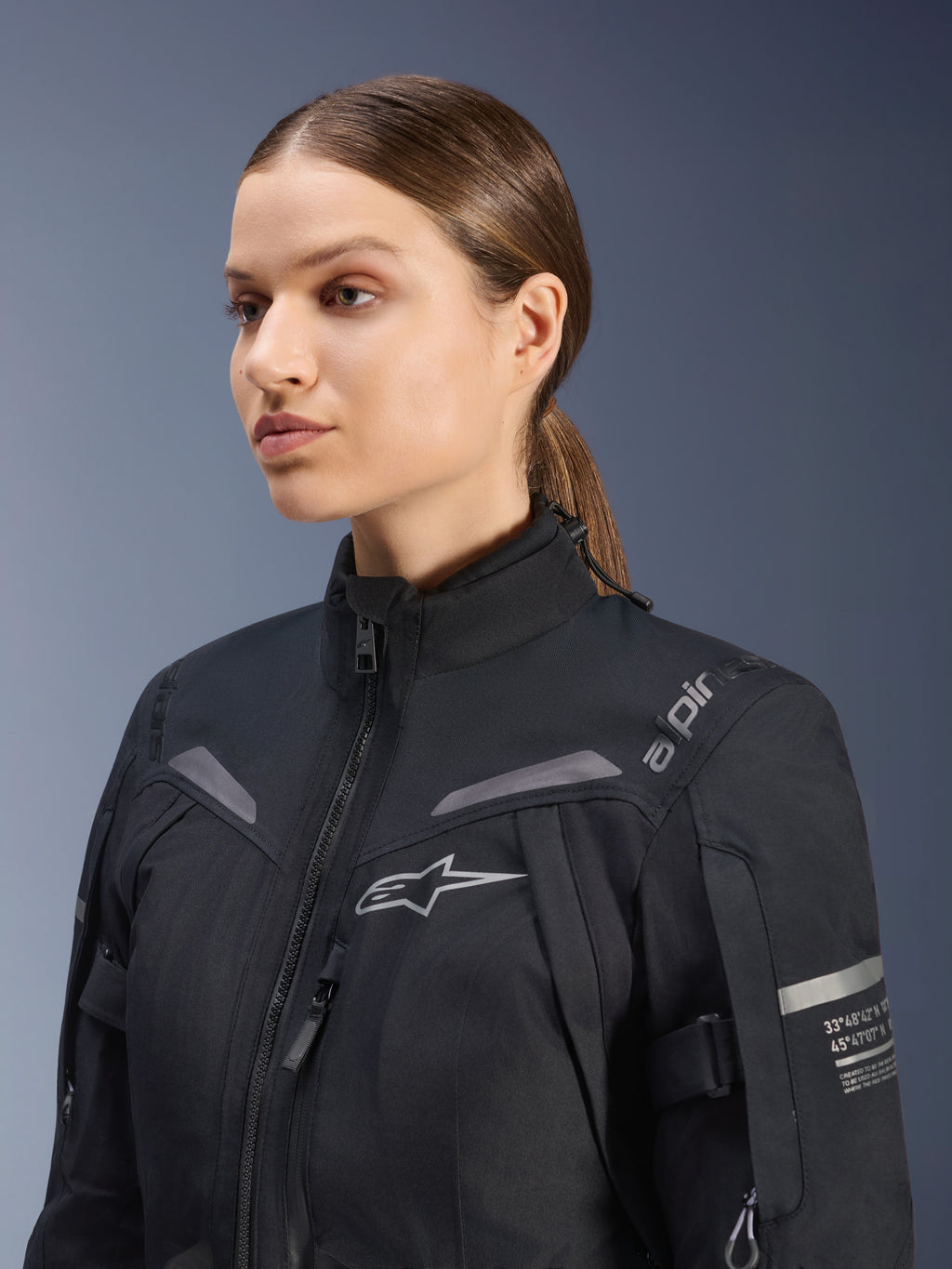 Alpinestars Women Stella ST-7 2L GORE-TEX Jacket, Black, featuring chest logo and technical coordinates on the arm, high-collar waterproof textile design for motorcycle touring, studio portrait of a female rider.