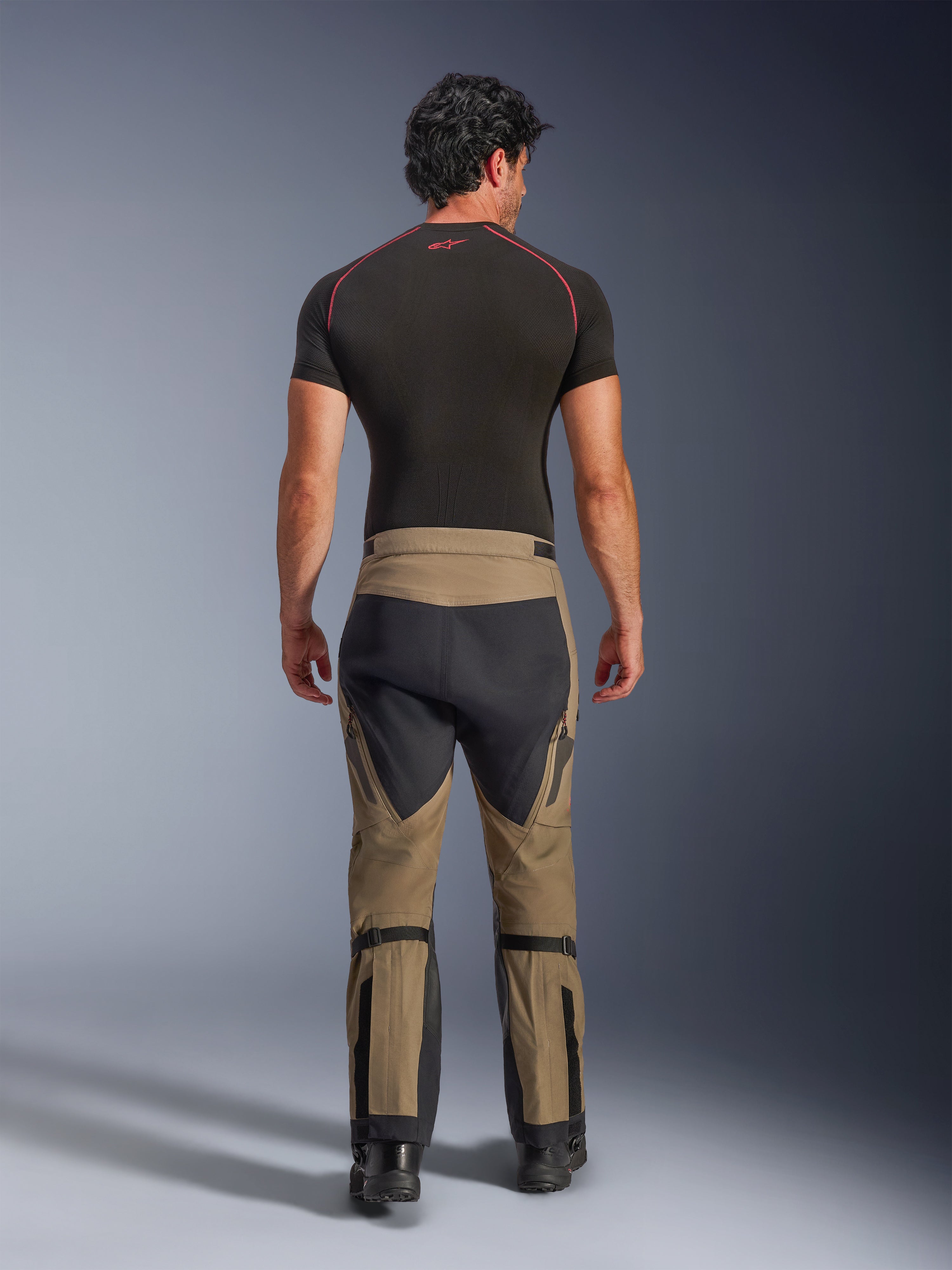Alpinestars Nazca 3L GORE-TEX PRO Pants, Walnut Black adventure motorcycle pants, rear view on a model wearing a black base layer and boots, featuring a two-tone design with calf adjusters and stretch panels.