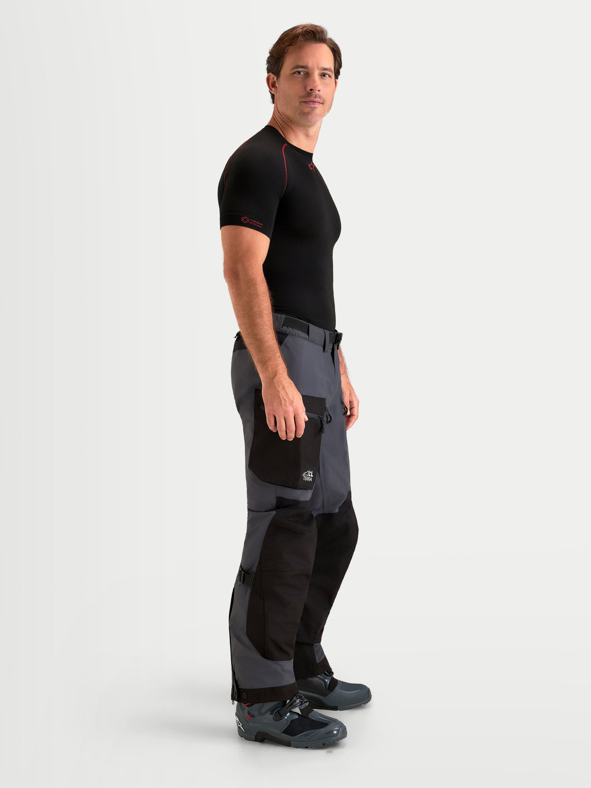 Alpinestars Arenis Gore-Tex Pants, men's adventure touring motorcycle pants in black and deep gray, side profile view worn by a model showing waterproof textile construction and cargo pocket.