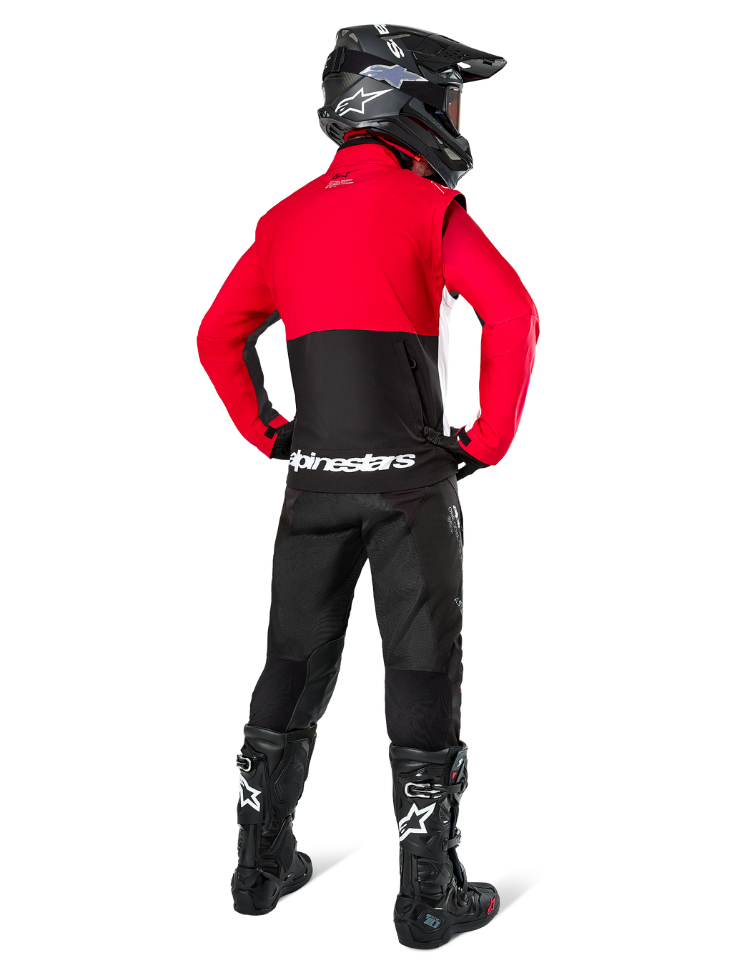 Motocross rider seen from behind wearing the Alpinestars Pro-Dura Jacket in Black, Bright Red, and White, paired with black pants, black helmet, and black off-road boots, featuring a red upper and black lower section with white Alpinestars branding across the back.
