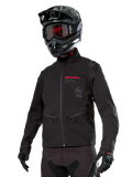 Alpinestars Lite-Dura Softshell Jacket, Black off-road motorcycle jacket with red branding and AS logo, worn with a black motocross helmet, red goggles, and black gloves, featuring zippered hand pockets and adjustable cuffs, designed for enduro riding.
