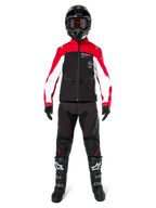 Motocross rider wearing the Alpinestars Lite-Dura Softshell Jacket in Black, Bright Red, and White, coordinated with black off-road pants, black and white boots, and a black helmet with goggles, complete gear setup for enduro racing