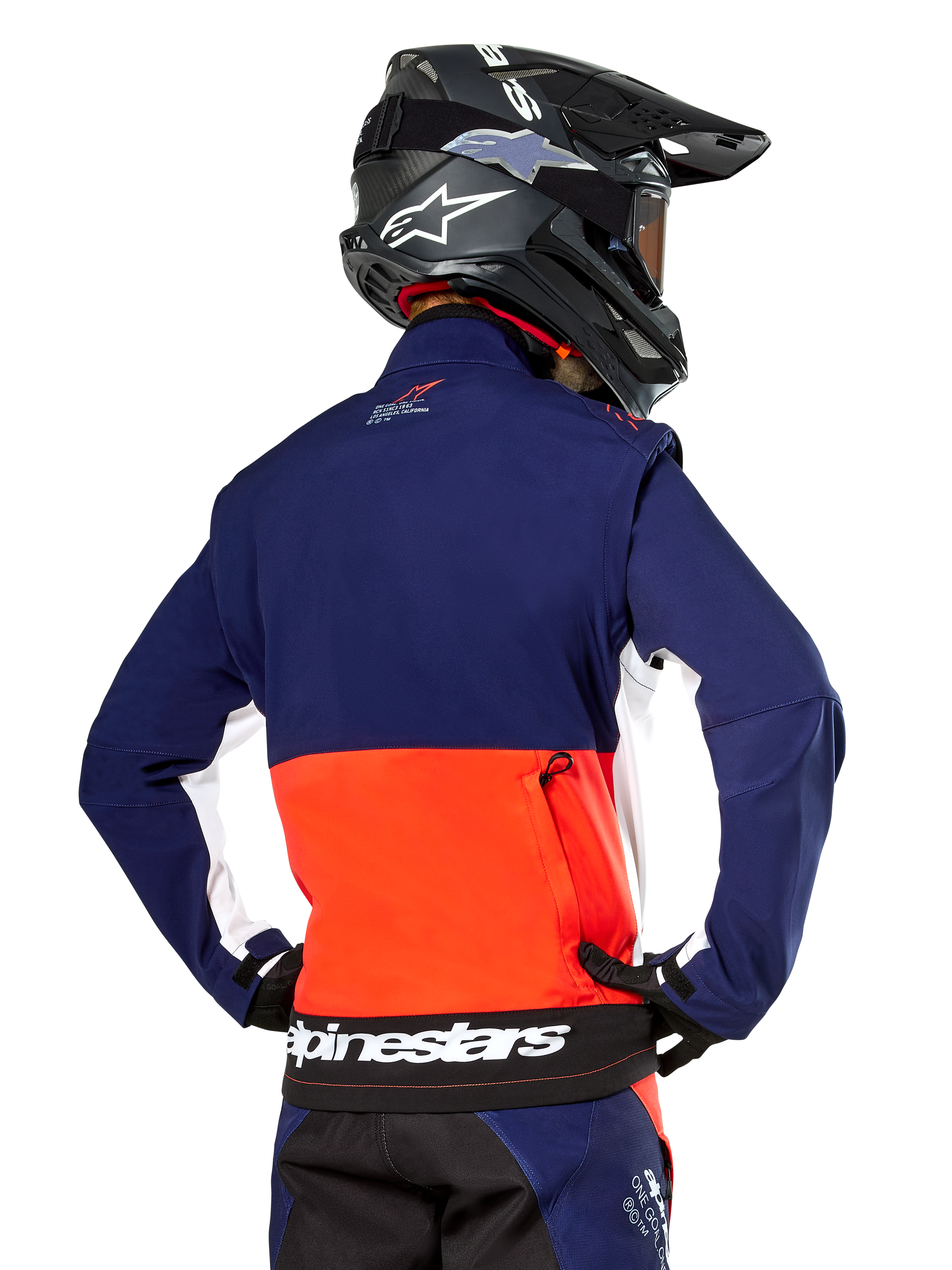 Alpinestars Lite-Dura Softshell Jacket, Navy Hot Orange and White, rear view worn by a motocross rider, featuring a large white logo on the back hem and zippered storage pocket, part of a complete off-road racing outfit.