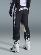 Rear view of Alpinestars 2026 Racer Air Riway Pants in Black and White, featuring prominent white 'astars' branding on the seat and leg, cream leather inner knee panels, worn with matching black and white motocross boots and jersey.