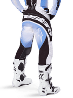 Alpinestars 2025 Techstar Melt Pants, Motocross Pants, Black Blue and White, rear view featuring bold Alpinestars wordmark across the seat and star logos on the legs, worn with white and black Tech 10 boots, professional off-road racing gear
