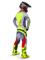 Motocross rider from a rear three-quarter view wearing Alpinestars 2025 Techstar Melt Pants in Bright Red and Gray, featuring a bold neon yellow logo across the seat, matching gray and neon yellow jersey, bright neon yellow boots, and a black helmet with neon goggles, professional off-road racing gear set.