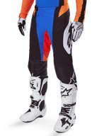 Alpinestars 2025 Techstar Melt Pants, Motocross Pants, Black with Blue and Orange accents, worn with white boots and matching jersey, featuring durable protective material and a sporty racing design