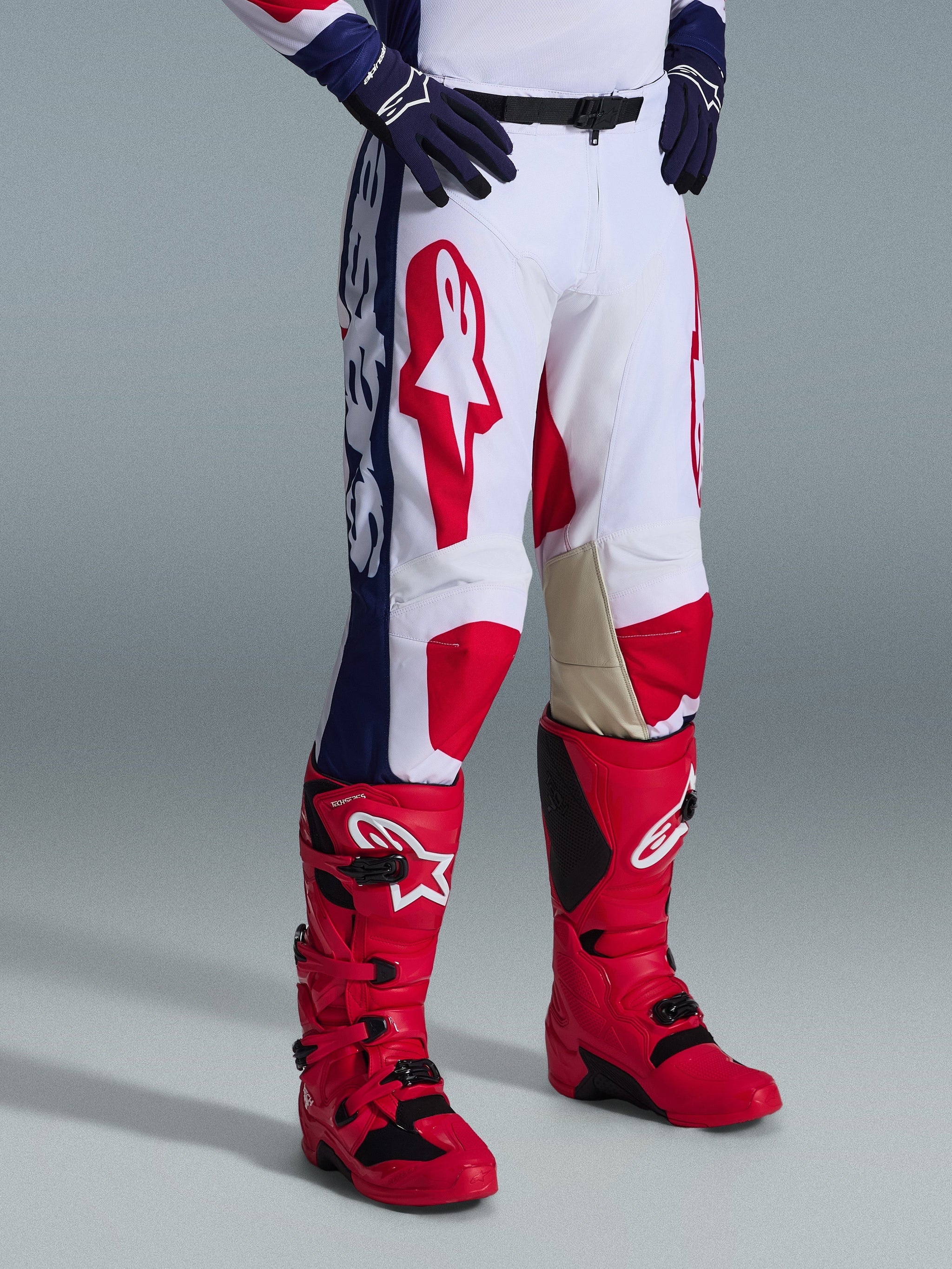 Alpinestars 2026 Racer Riway Pants, Motocross Pants, White Blue Red, featuring bold red logos on thighs and blue side panels with white branding, worn with red boots and dark blue gloves, ergonomic design for off-road racing