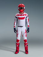 Motocross rider wearing the Alpinestars 2026 Racer Riway Gear Set, White jersey with red "astars" branding and blue side panels, white pants with red graphics, red racing helmet and boots, navy blue gloves, complete coordinated motocross racing outfit