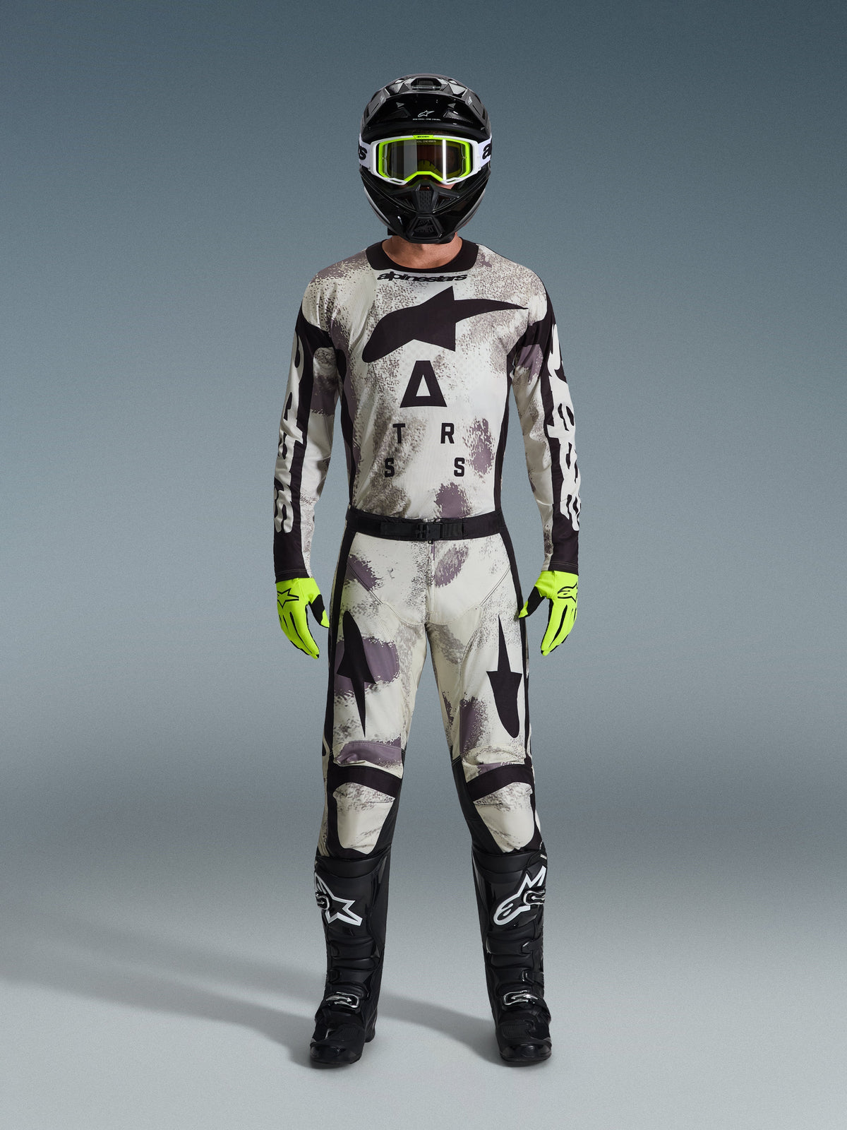 Motocross rider wearing 2026 Racer Lahnd Jersey and matching pants in Sand Camo, black helmet with neon yellow goggles, neon yellow gloves, and black boots, complete Alpinestars off-road racing gear set