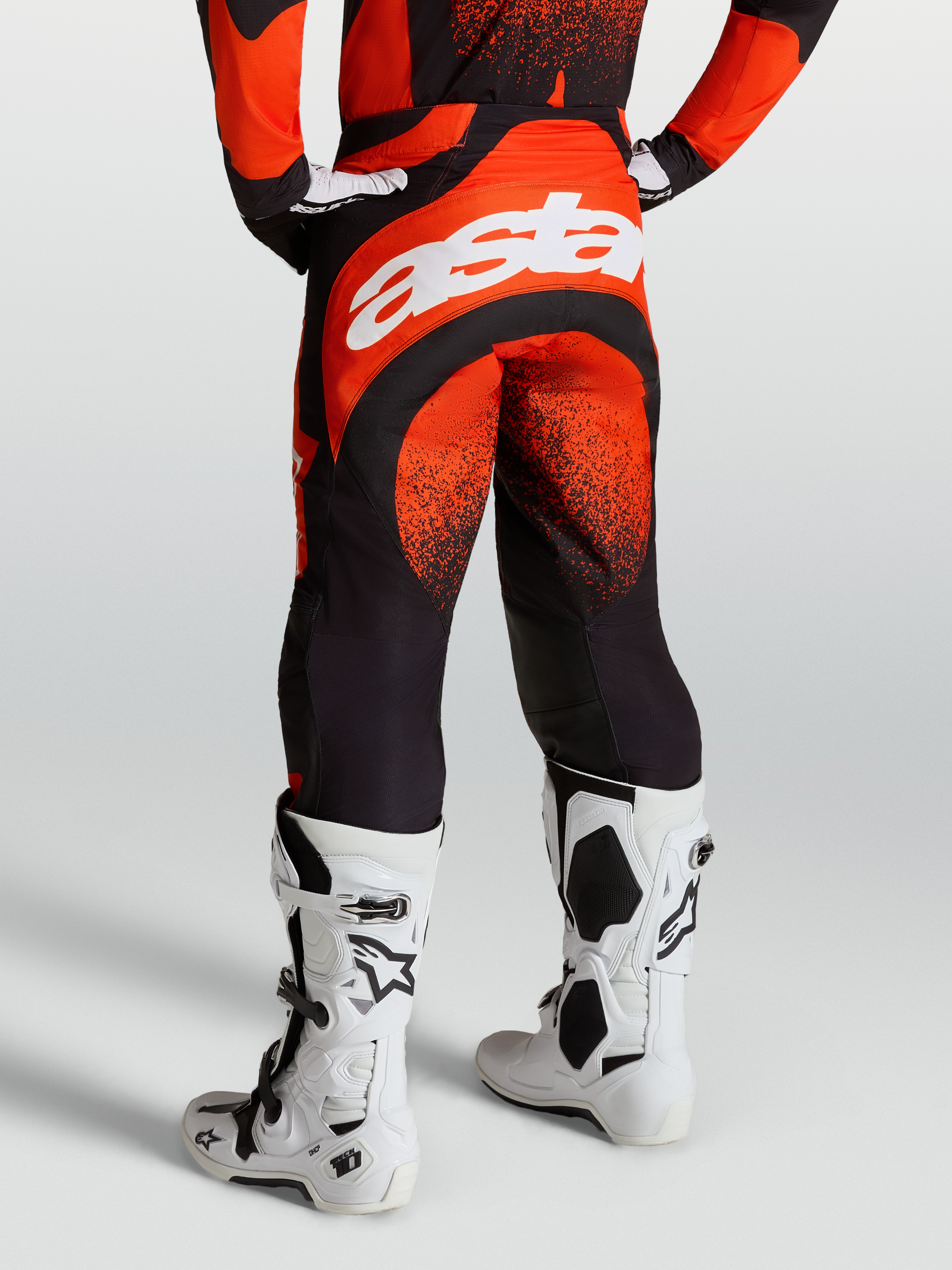 Alpinestars Techstar Swan Pants, Motocross Racing Pants for Men, Cardinal Red and Black, durable stretch chassis with white Astar branding on the rear, shown on-model with white Tech 10 boots.
