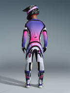 Motocross rider seen from behind wearing complete racing gear, purple and pink gradient jersey, Alpinestars 2026 Supertech AFD Vista Pants in White Purple and Black, black helmet with purple goggles, white and purple boots, coordinated off-road racing kit.