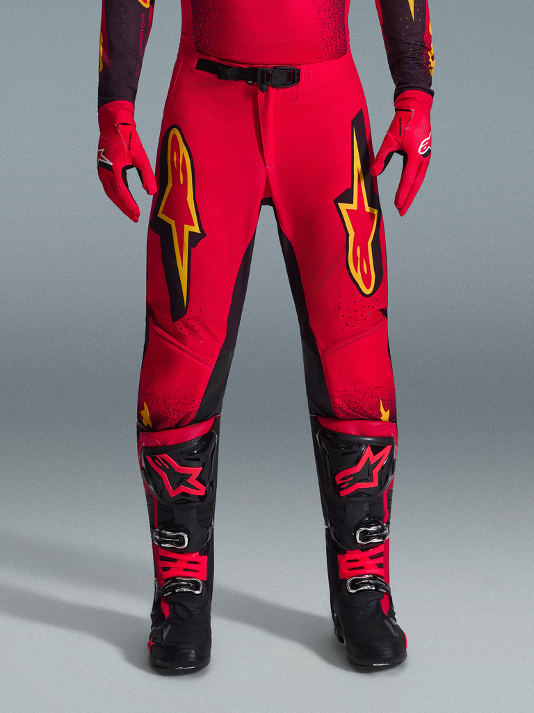Alpinestars 2026 Supertech Scenz Pants, Motocross Pants, Red Black and Yellow, pro-level athletic fit with large yellow star logos on the thighs, paired with matching red gloves and black and red technical boots, designed for elite off-road racing performance