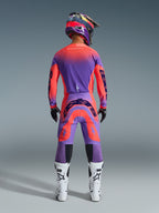 Alpinestars 2026 Supertech Scenz Pants, Motocross Pants, Hot Coral and Purple, rear view of motocross rider wearing a complete racing gear set, featuring vibrant gradient design with bold rear logos, paired with a matching jersey, helmet, and white boots.