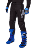 Alpinestars 2025 Racer Graphite Pants, Black Motocross Pants with white and gray graphics, worn with bright blue motocross boots and matching blue gloves, durable performance fabric for off-road riding