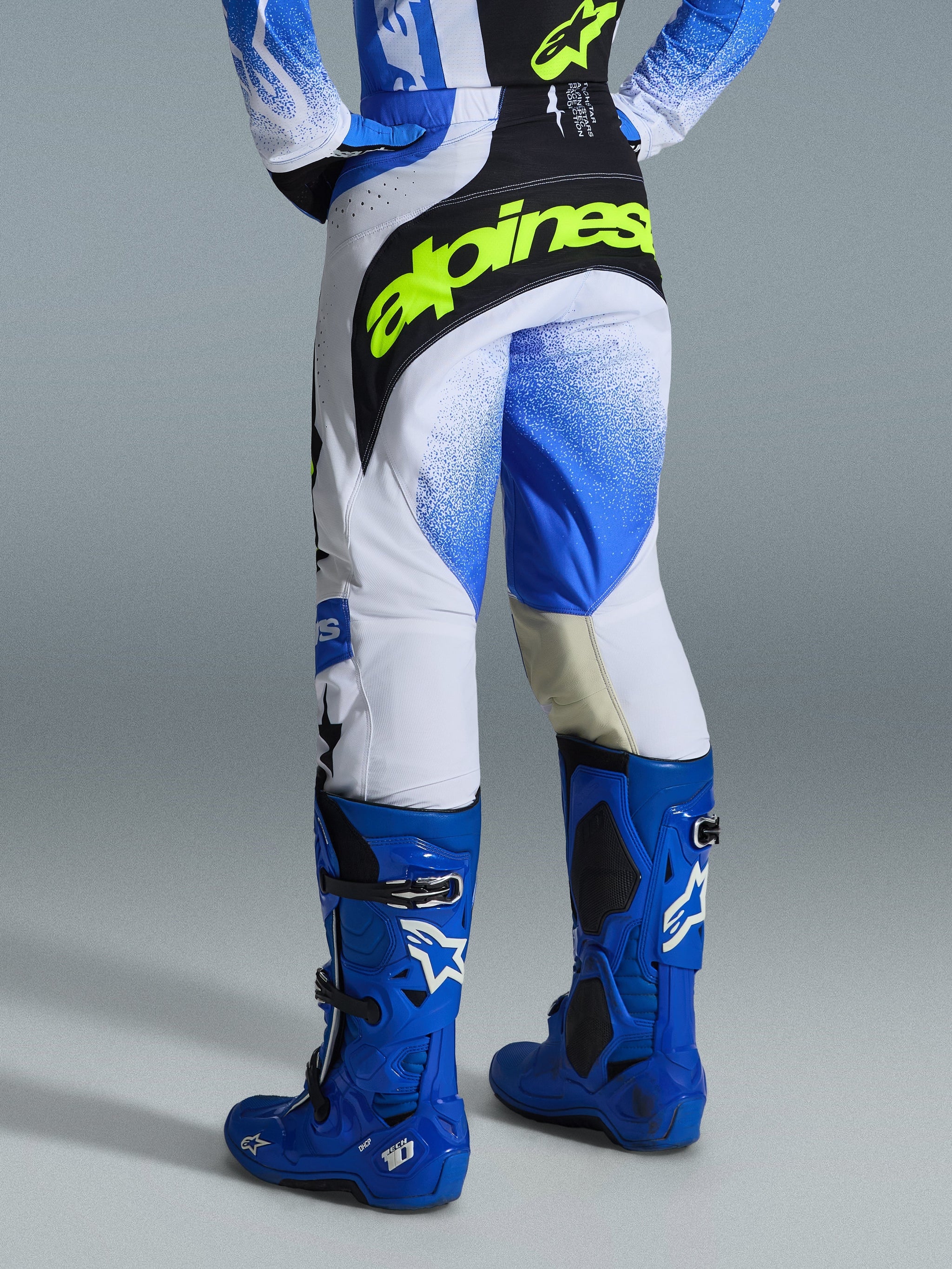 Alpinestars 2026 Techstar Knif Pants, Motocross Pants, Ucla Blue Black and Yellow Fluo, rear view showing a bold neon yellow Alpinestars logo across the back, white chassis with blue gradient graphics, worn with high-performance bright blue motocross boots.