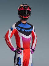 Alpinestars 2026 Techstar Knif Jersey, Motocross Jersey, white with red, blue, and pink gradient patterns, featuring bold blue branding on the chest, worn with coordinated helmet and gloves, athletic racing design for off-road performance