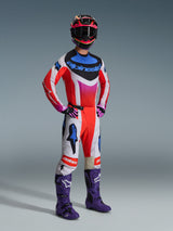 Motocross rider wearing complete Alpinestars racing gear, 2026 Techstar Knif Jersey in white and red with blue and pink accents, matching motocross pants, purple boots, and a multi-colored helmet, coordinated professional outfit for off-road performance