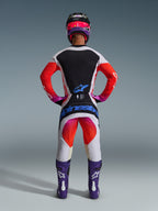 Alpinestars 2026 Techstar Knif Gear Set, complete motocross gear seen from behind, White and Black jersey with red gradient sleeves, White pants with red and pink accents, coordinated with purple boots and pink helmet, bold blue branding, professional off-road racing kit
