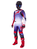 Motocross rider wearing complete racing gear, 2025 Fluid Wurx Pants and matching jersey in Purple Bright Red and White, large red Alpinestars logo, red boots and gloves, black helmet with blue goggles, coordinated outfit for off-road racing
