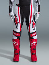 Alpinestars 2026 Techstar Nomur Pants, Motocross Pants, Black White and Red, worn with matching red boots and white gloves, featuring bold red logos on the thighs and 'astars' branding on the knees, multi-panel racing design for off-road performance