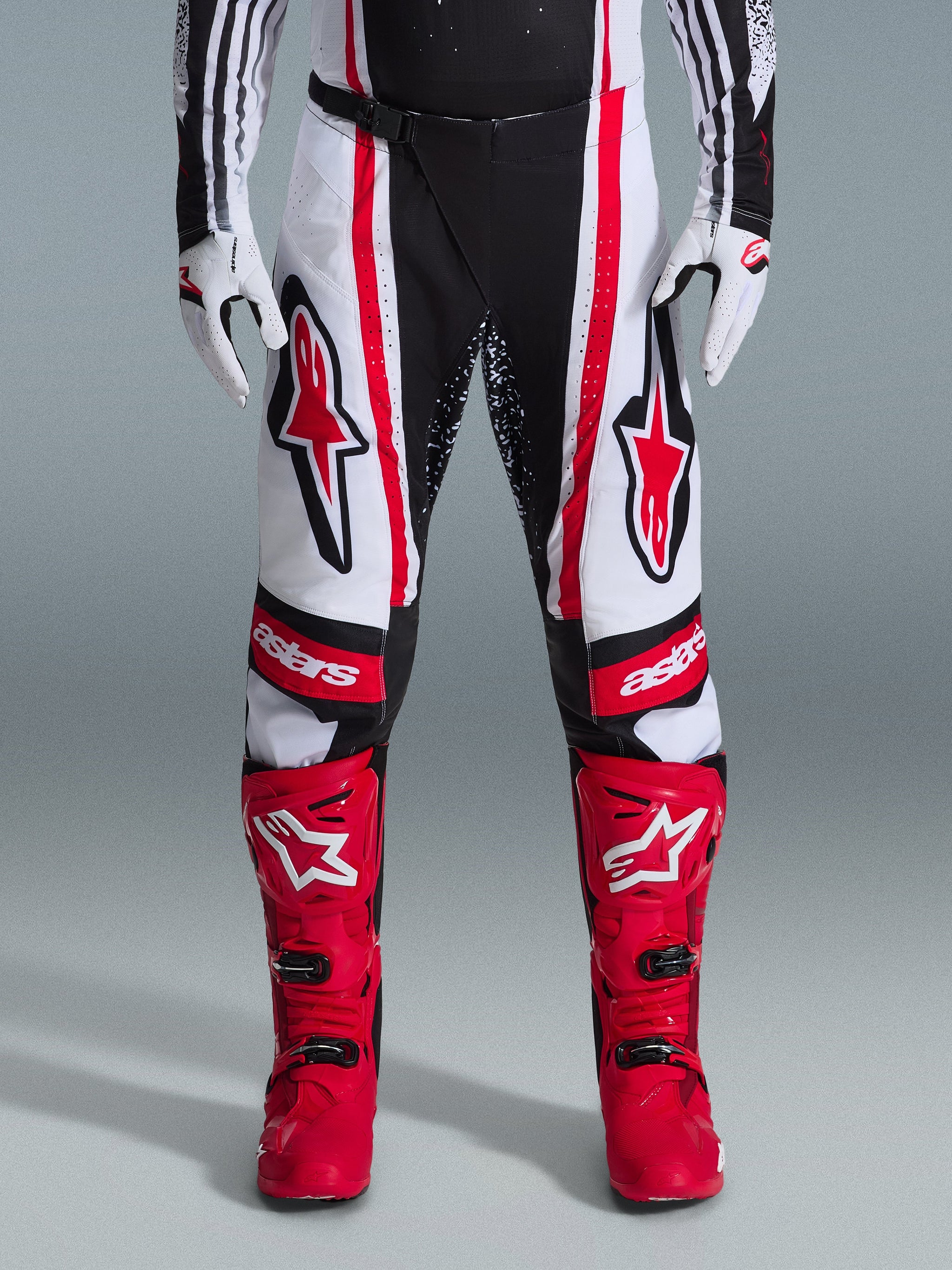 Alpinestars 2026 Techstar Nomur Pants, Motocross Pants, Black White and Red, worn with matching red boots and white gloves, featuring bold red logos on the thighs and 'astars' branding on the knees, multi-panel racing design for off-road performance
