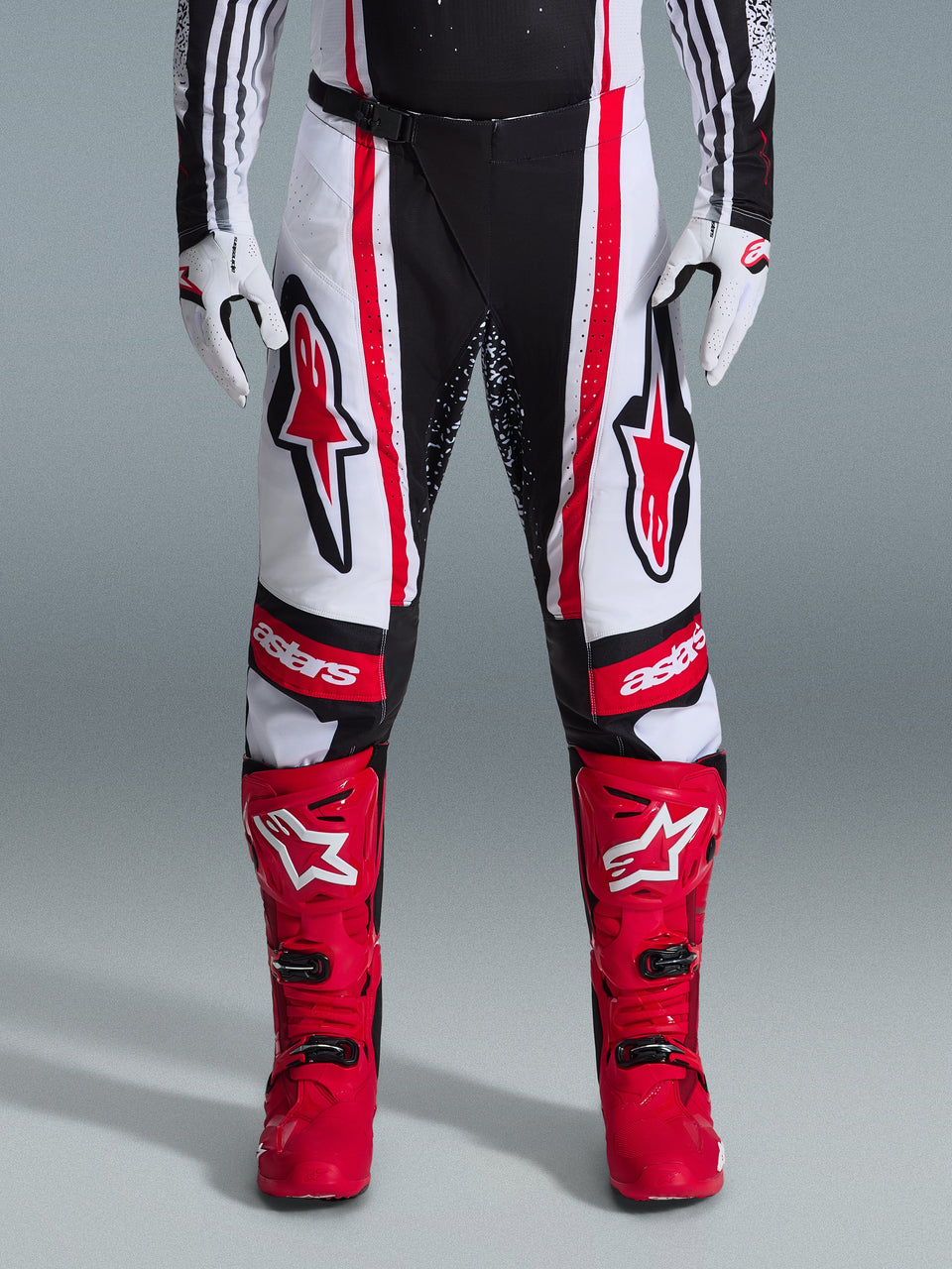 Alpinestars 2026 Techstar Nomur Pants, Motocross Pants, Black White and Red, worn with matching red boots and white gloves, featuring bold red logos on the thighs and 'astars' branding on the knees, multi-panel racing design for off-road performance