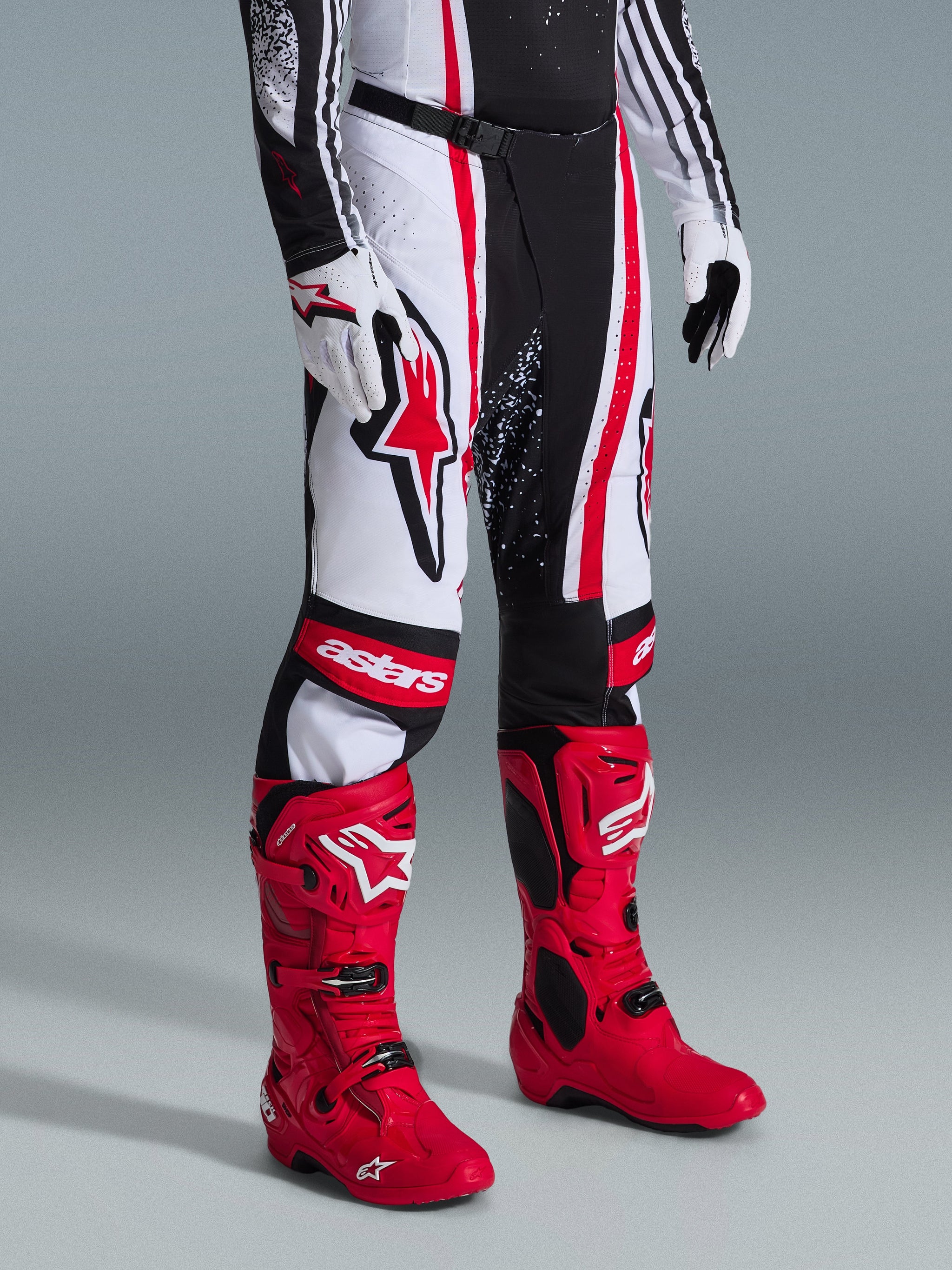 Alpinestars 2026 Techstar Nomur Pants, Motocross Pants, Black White Red, worn with vibrant red racing boots and white gloves, featuring bold vertical stripes, a large red star logo on the thigh, and reinforced knee panels for off-road performance.