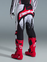 Alpinestars 2026 Techstar Nomur Pants, Motocross Pants, Black White and Red, rear view shown on a rider with matching red boots, featuring a bold red and white 'astars' logo on the seat and speckled graphic patterns, professional off-road racing gear