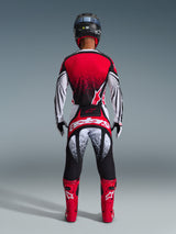 Rear view of a motocross rider wearing Alpinestars 2026 Techstar Nomur Pants in Black White Red, featuring bold branding on the seat and speckled graphics, paired with a matching red jersey and bright red boots for a complete off-road racing kit