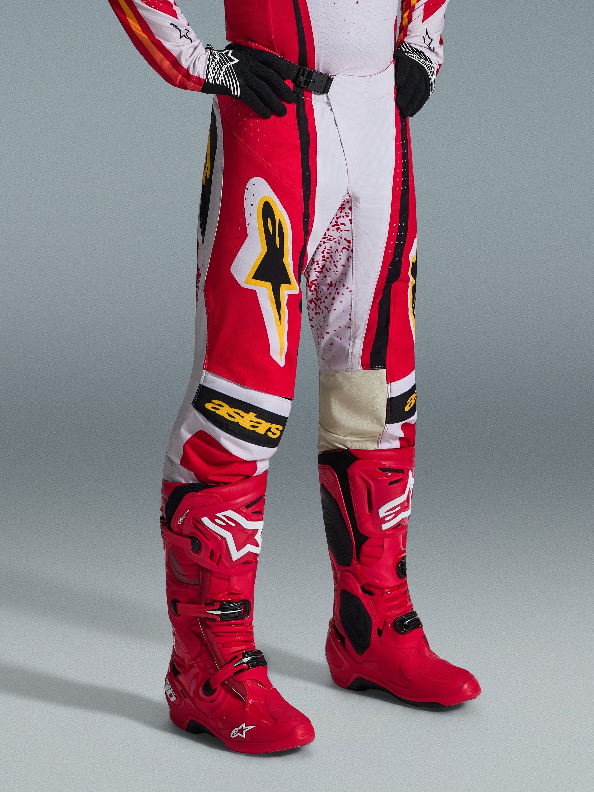Alpinestars 2026 Techstar Nomur Pants, Motocross Pants, Red White and Black with yellow accents, worn with matching red motocross boots and black gloves, featuring yellow Alpinestars logo and "astars" branding on the knees, professional off-road racing gear.