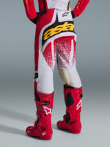 Rear view of a motocross rider wearing Alpinestars 2026 Techstar Nomur Pants in red and white with a bold yellow logo on the seat, paired with bright red Tech 10 motocross boots, studio shot against a gray background.