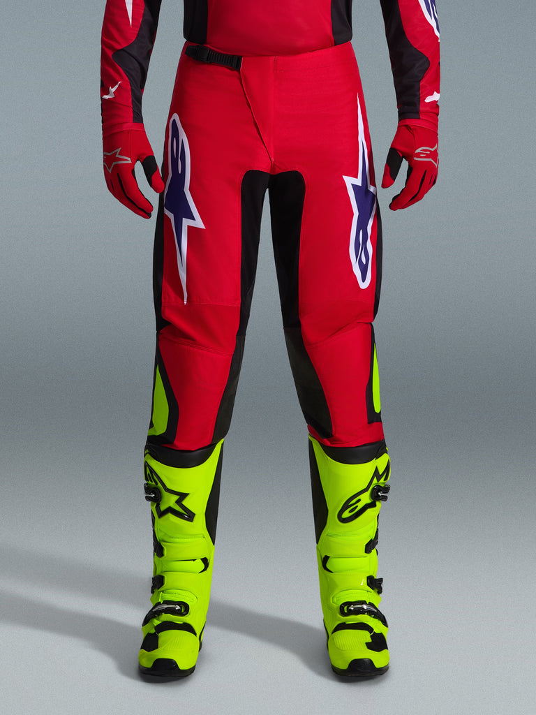 Alpinestars 2026 Fluid Grid Pants, Motocross Pants, Red with black panels and neon yellow accents, featuring large white and purple star logos on thighs, worn with red gloves and neon yellow boots, durable construction for off-road racing