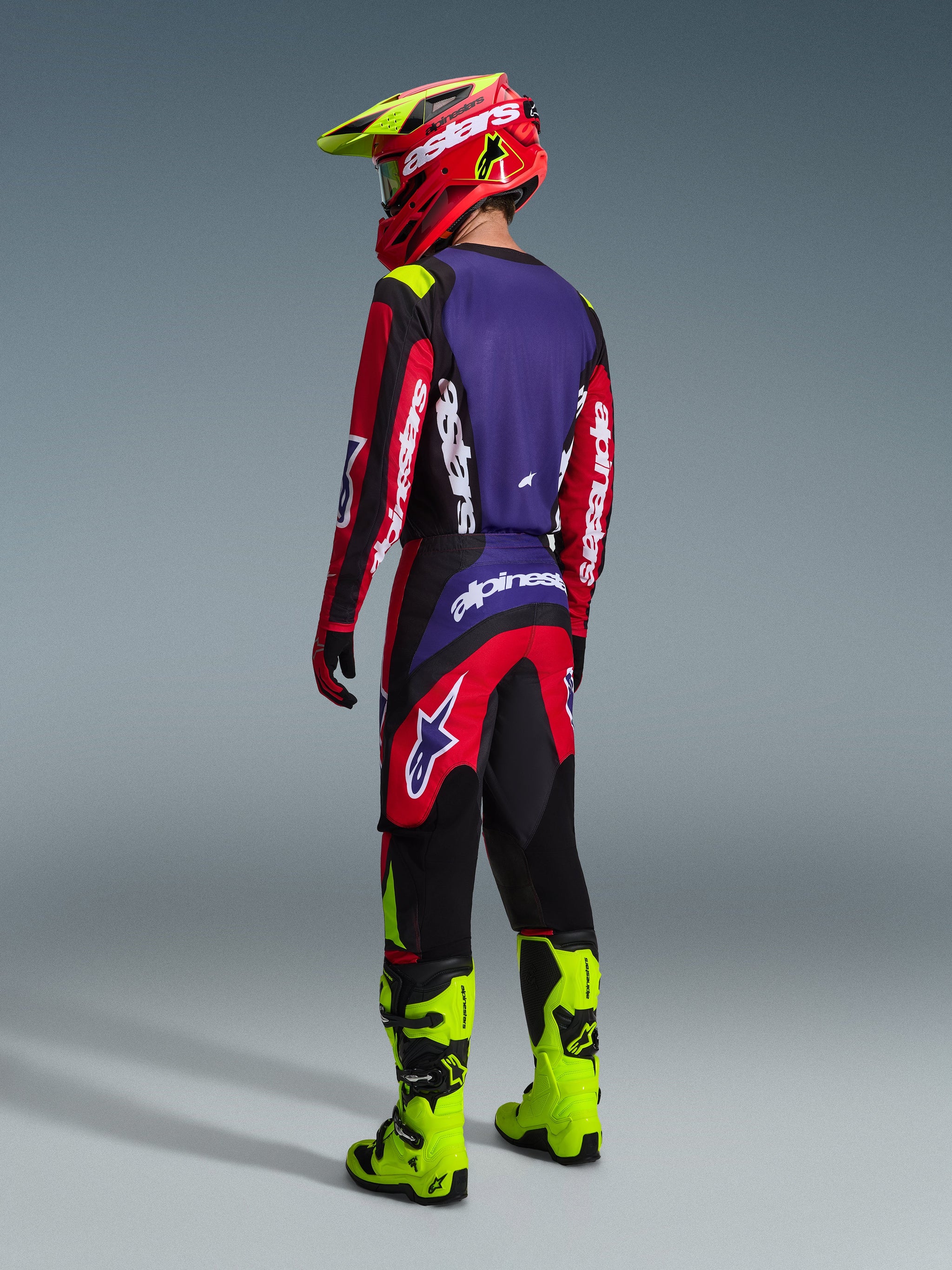 Alpinestars 2026 Fluid Grid Pants, Motocross Pants, Red Black and Purple, worn by a rider from behind with matching jersey and fluo yellow boots, featuring bold branding and ergonomic design for off-road performance.