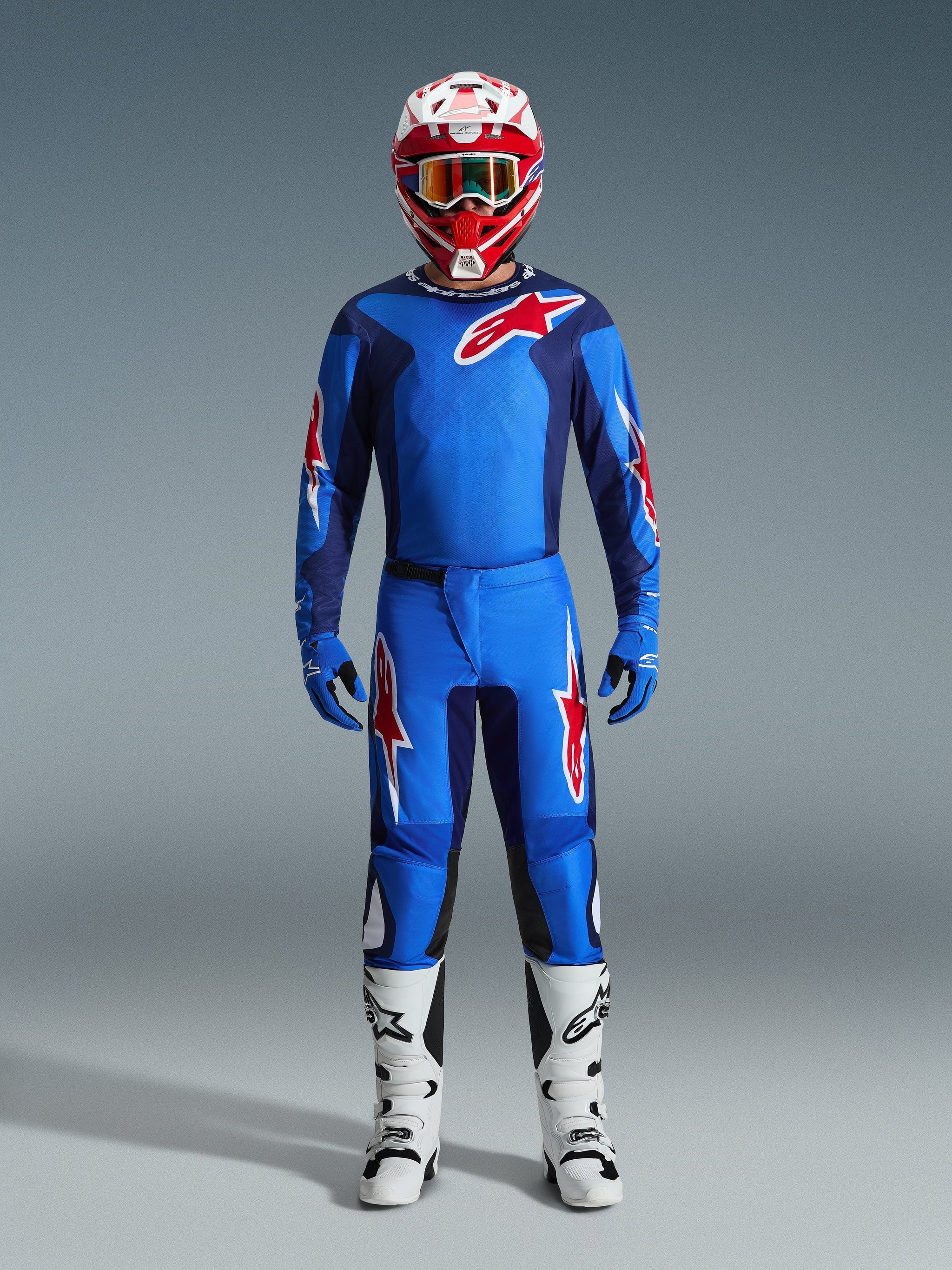 Motocross rider wearing Alpinestars 2026 Fluid Grid Pants in Blue and Red, matching blue jersey with a red Astars logo, red and white helmet with goggles, blue gloves, and white motocross boots, complete coordinated off-road racing gear.