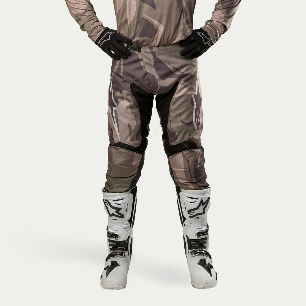 Alpinestars 2024 Racer Tactical Pants, Motocross Pants, Military Green Camo Brown, featuring large white Alpinestars logos on the thighs and black inner leg panels, worn with white and black motocross boots and black gloves, matching camouflage jersey, front view.