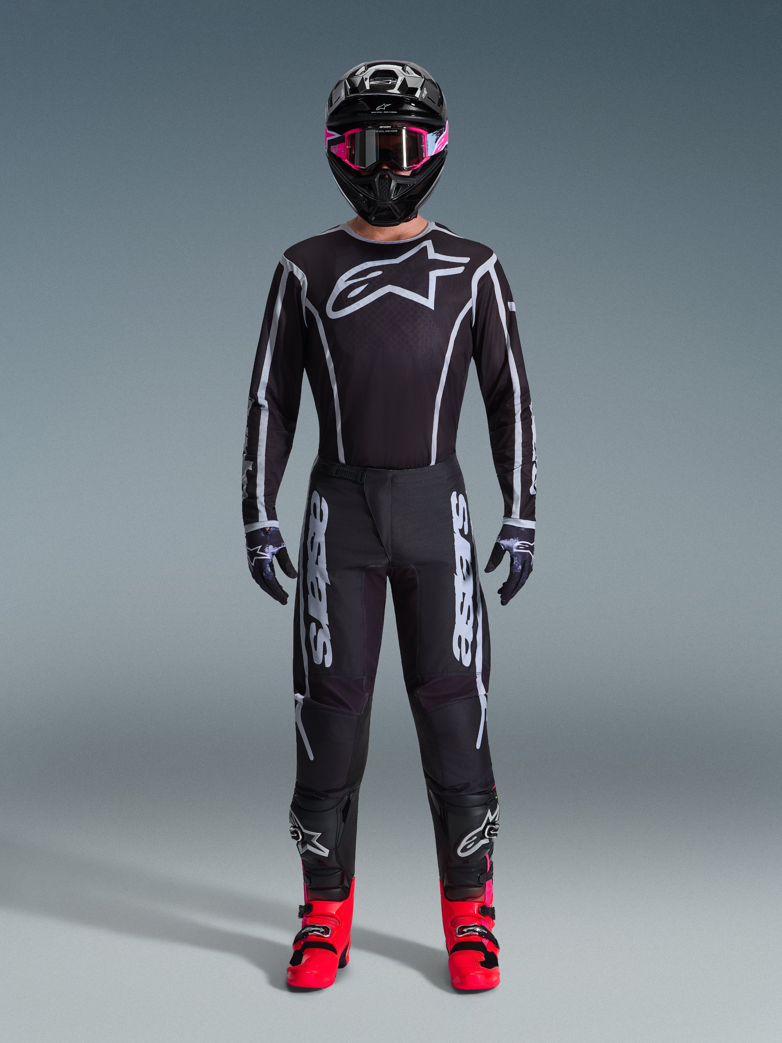 Alpinestars 2026 Fluid Apex Gear Set, Motocross Outfit, Black with Gray accents, jersey featuring large white Astars logo, matching pants with bold branding, black helmet with pink goggles, and bright red boots, complete off-road racing kit