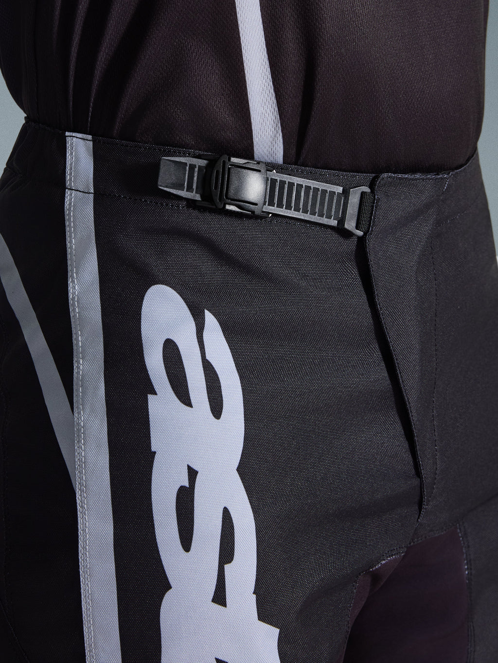 Alpinestars 2026 Fluid Apex Pants, Motocross Pants, Black and Gray, close-up detail of the integrated ratchet closure system for a secure fit, featuring white logo graphics on durable 600D polyfabric.