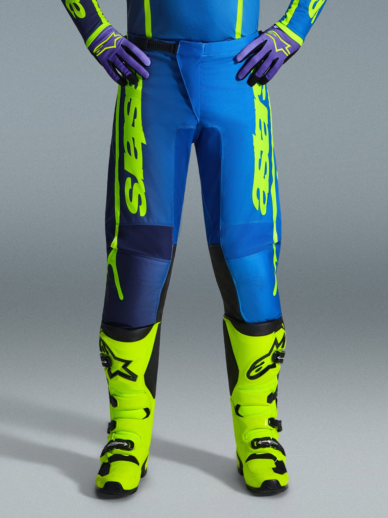Alpinestars 2026 Fluid Apex Pants, Motocross Pants, Blue and Yellow Fluo, worn with matching fluo yellow boots and purple gloves, bold yellow branding on the sides, ergonomic design for off-road racing